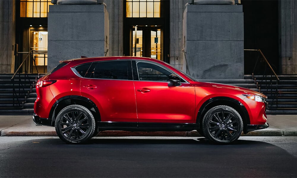 Un Mazda CX-5 rouge vibrant cristal stationné dans une rue en ville, vu de profil.