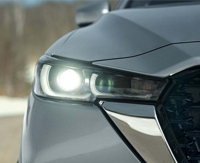 Close up of front right side headlight, hood, front panel and side of grille of Machine Grey Metallic Mazda CX-5.  