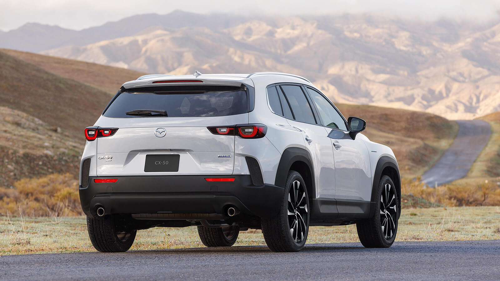 Back ¾ of Wind Chill Pearl CX-50 Hybrid parked on paved road in tundra environment, mountains in background.