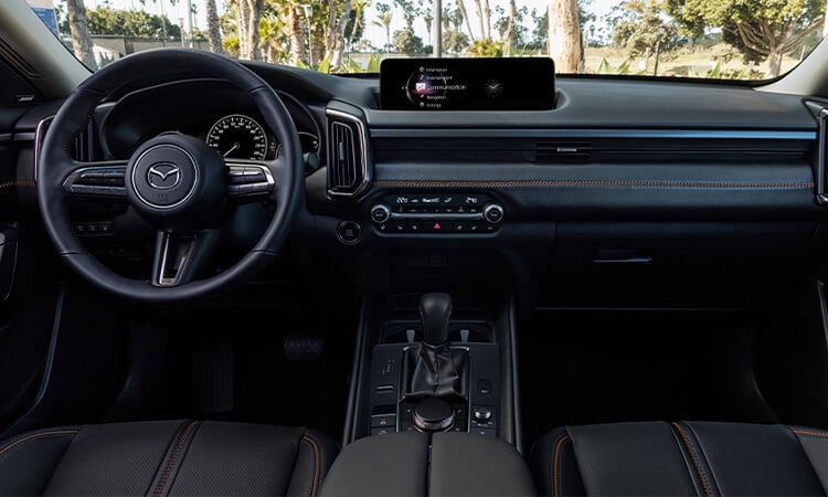 Interior centre view looking forward showing seats, cockpit, dash and console in black leather with red stitching.