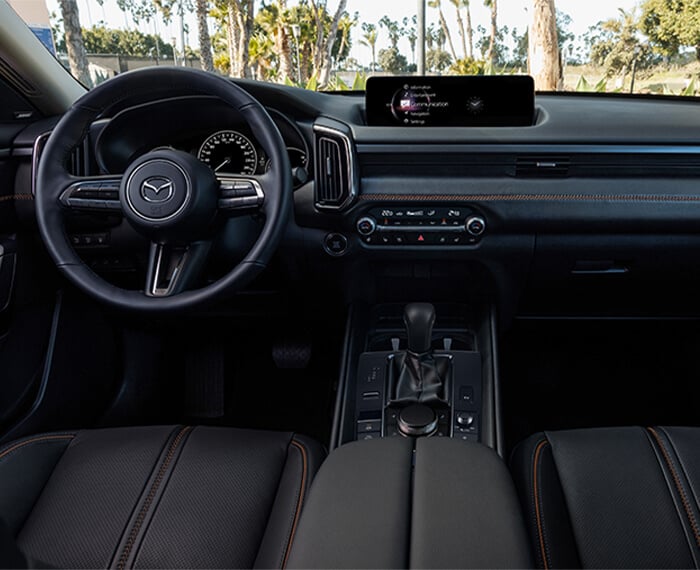 Interior centre view looking forward showing seats, cockpit, dash and console in black leather with red stitching.