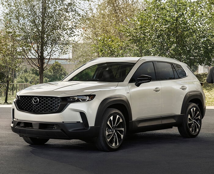 CX-50 Hybrid parked front ¾ in residential area. A man and woman are going for jog passing the rear of the vehicle.