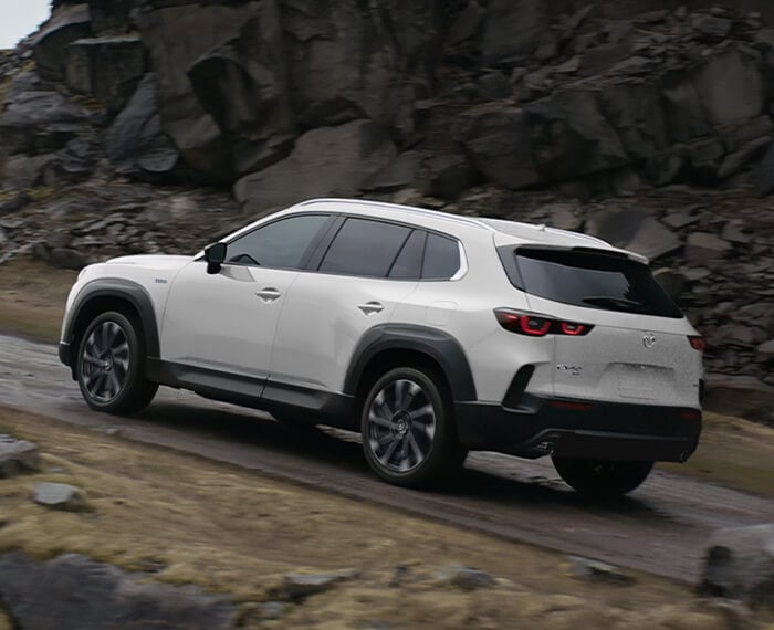 Wind Chill Pearl Mazda CX-50 Hybrid from back ¾ climbing a paved mountain road.