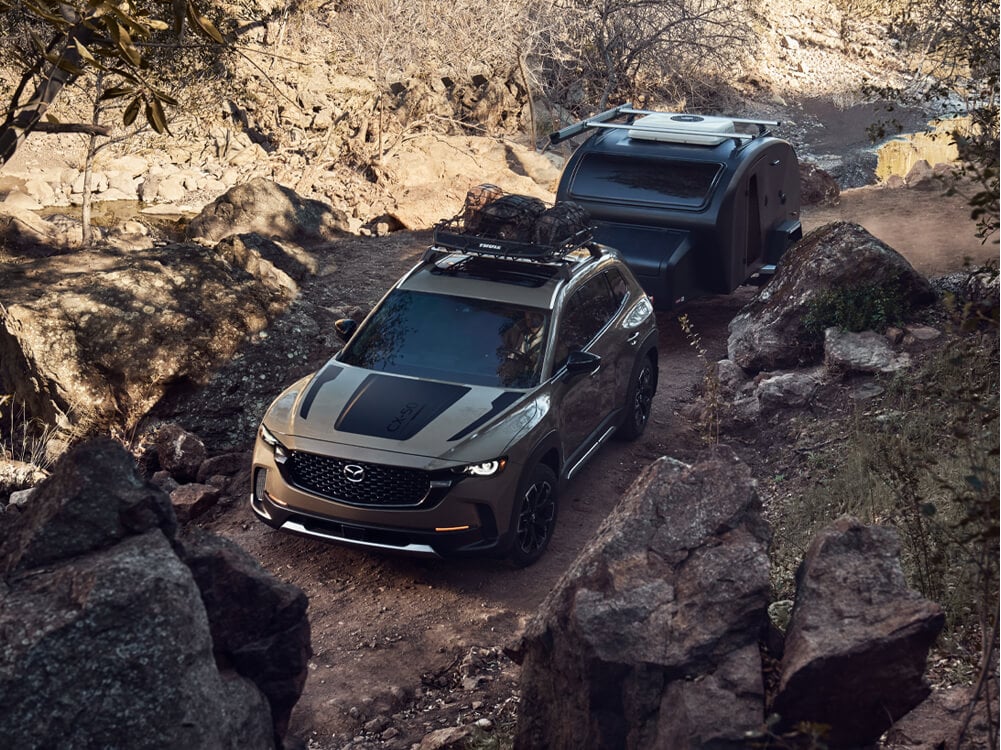 High camera angle of Zircon Sand Metallic Meridian trim CX-50 pulling stylish camper through rocky gully