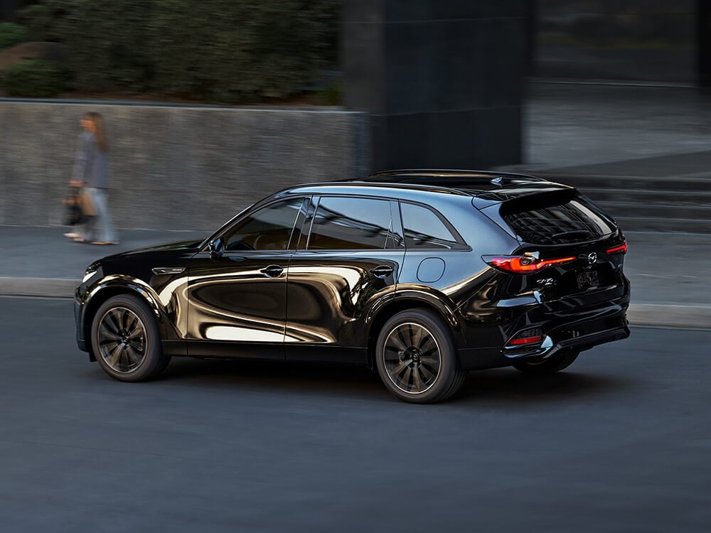 CX-70 Inline 6 Turbo reflects the surrounding buildings as it passes a pedestrian in daylight.