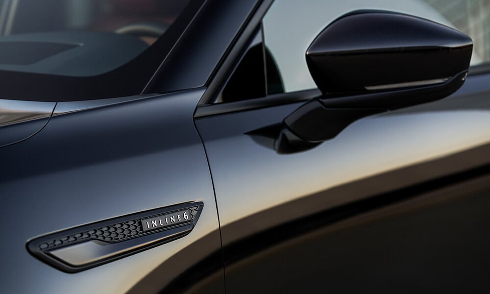 Close up of Driver’s side mirror, the CX-70 the evening light with the “Inline 6” badge just below the hood’s corner.