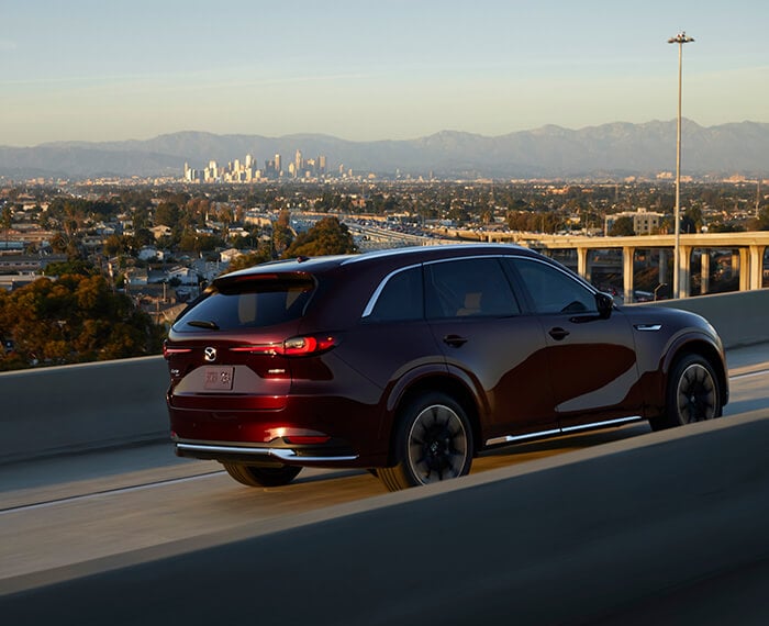 Un CX-90 rouge artisan roule vers le coucher du soleil sur un pont autoroutier en béton.