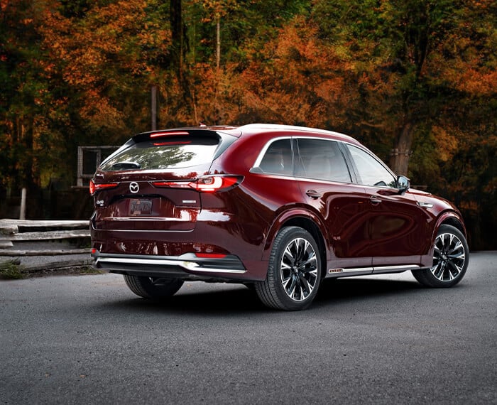 Sunlight gleaming off of the back left wheel well and taillight of an Artisan Red CX-90.