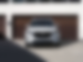  Un CX-90 hybride rechargeable blanc branché à une borne domestique dans l’allée d’une maison avec une porte de garage en bois.