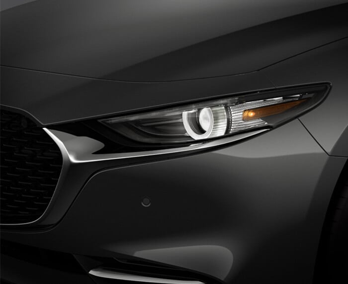 Close-up of driver’s side headlight and bumper of Machine Grey Metallic Mazda3. 