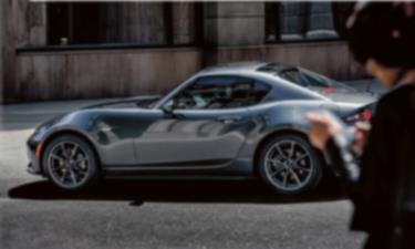 A metallic, reflective MX-5 RF sits parked on a city street.