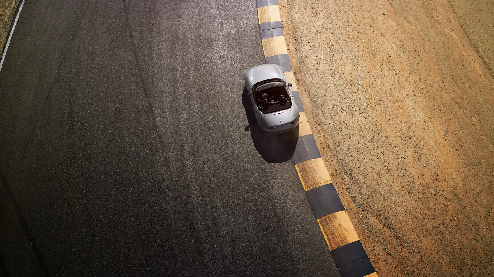 Vue en plongée d’une MX-5 ST roulant sur une route près d’un terrain sablonneux.