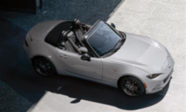 A sliver MX-5 ST parked half in the shade and half in sunlight.