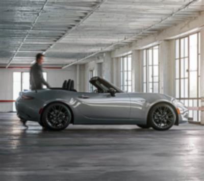 A person walks near the back of an MX-5 ST parked in an interior space.