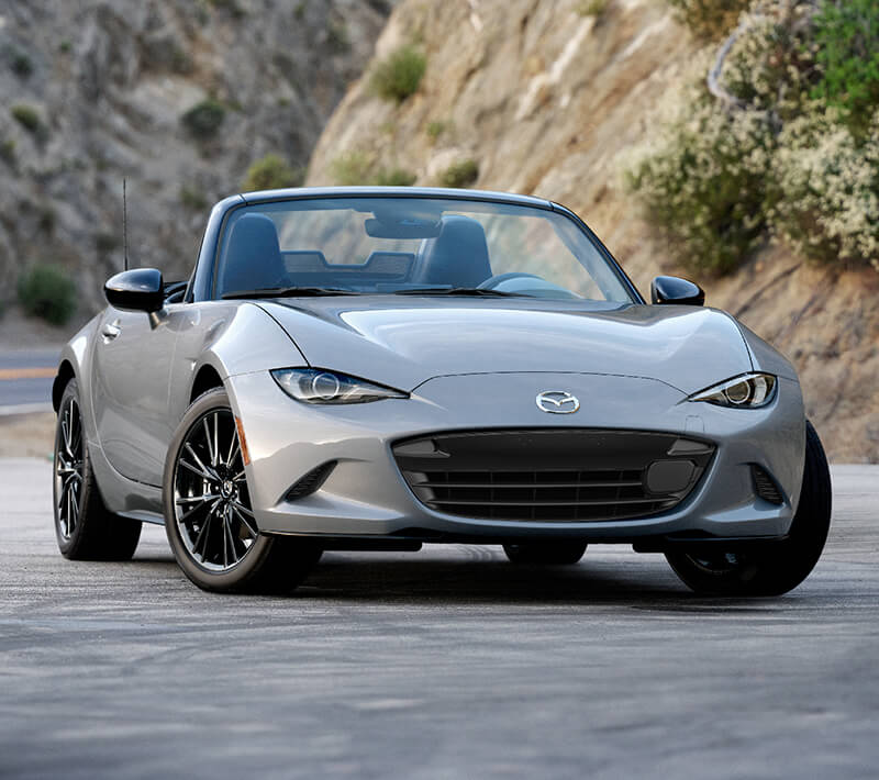 Une MX-5 ST argent roule sur une route traversant les montagnes.