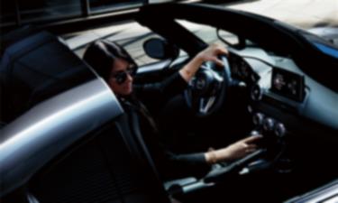 Interior view of the MX-5 ST driver’s side seat with steering wheel and dashboard featuring black leather trim details.