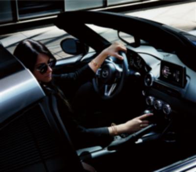 Interior view of the MX-5 ST driver’s side seat with steering wheel and dashboard featuring black leather trim details.