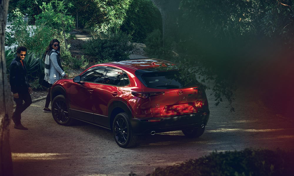 Une femme ouvre la portière côté conducteur d’un Mazda CX-30 rouge vibrant cristal métallisé