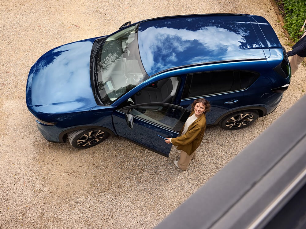 Overhead view of a Navy Blue Mica Mazda CX-5. A woman opens the driver's door while a man opens the trunk.