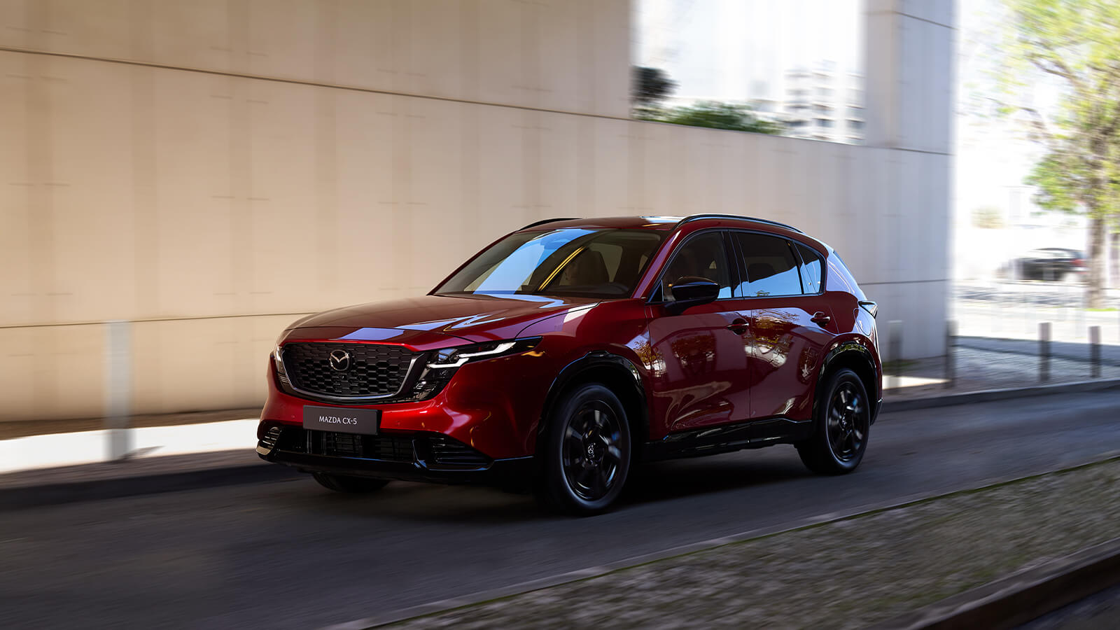 A Soul Red Crystal Mazda CX-5 shown from the front side profile, with a blurred city road in the background.