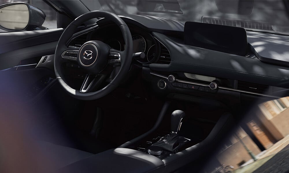 Intérieur d’une Mazda3 vue de l’extérieur à travers la fenêtre ouverte du siège passager avant.