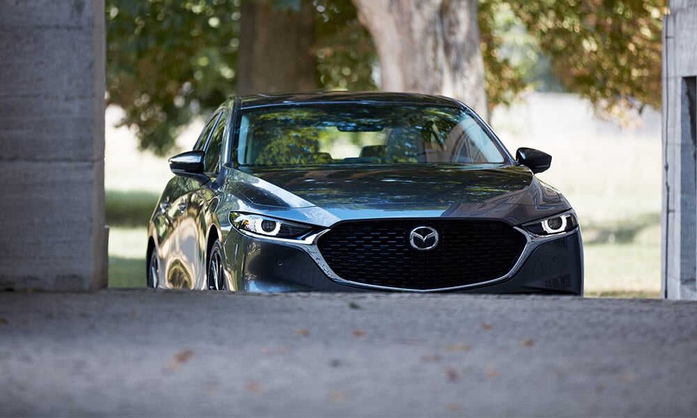 Vue de l’avant d’une Mazda3 bleu cristal foncé mica avec les roues avant partiellement obscurcies par la route semblant rouler vers le haut d’une colline.
